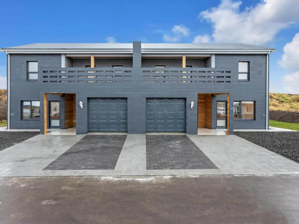 Symmetric modern residential facade featuring dark grey self-coloured fibre cement panels around garage and upper terrace