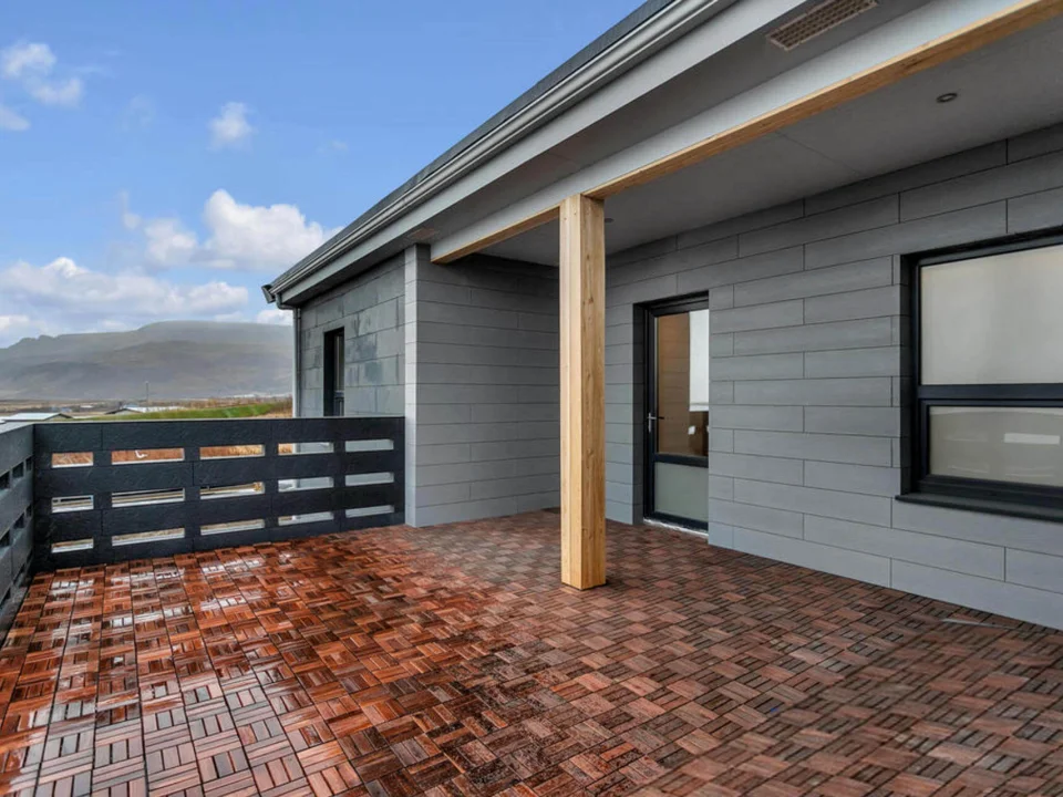 Close-up veranda facade with ash-grey through-coloured stone-textured fibre cement panels and dark window frames