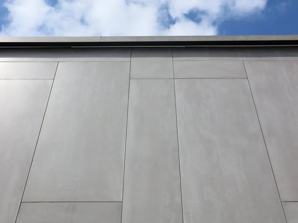 Upward architectural facade view of smoke-grey through-coloured stone-textured fibre cement rainscreen panels with crisp open vertical and horizontal joints