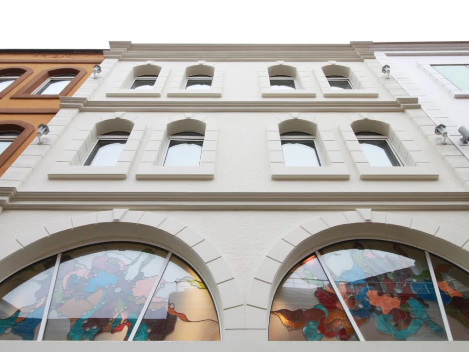 Upward architectural view of a cream-painted classical urban building facade featuring bold 20 mm fibre cement floor-band cornices, crown moulding and arched window trims