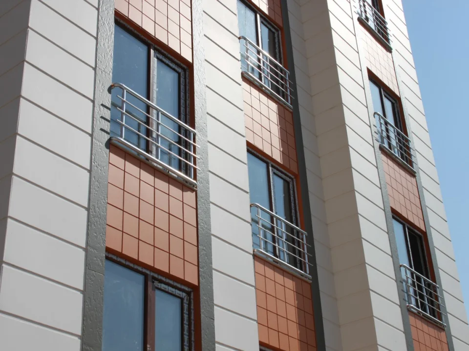 Close-up residential facade combining light grey horizontally grooved fibre cement panels on vertical piers with terracotta small-block stone panels between windows