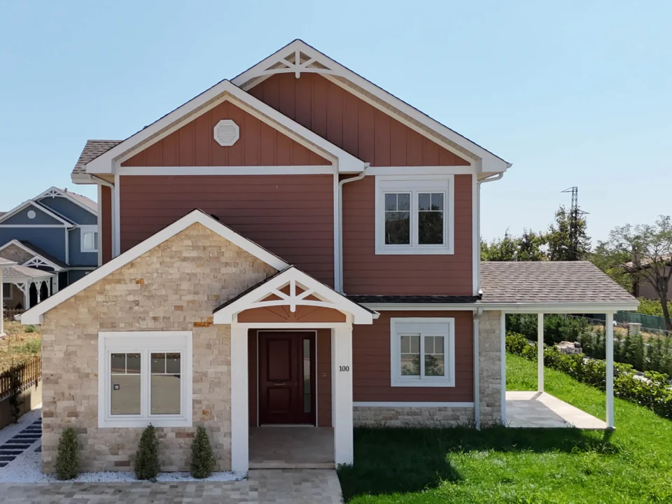 Two-storey detached family house clad in terracotta-red painted horizontal fibre cement lap siding, white window trims and stone gable