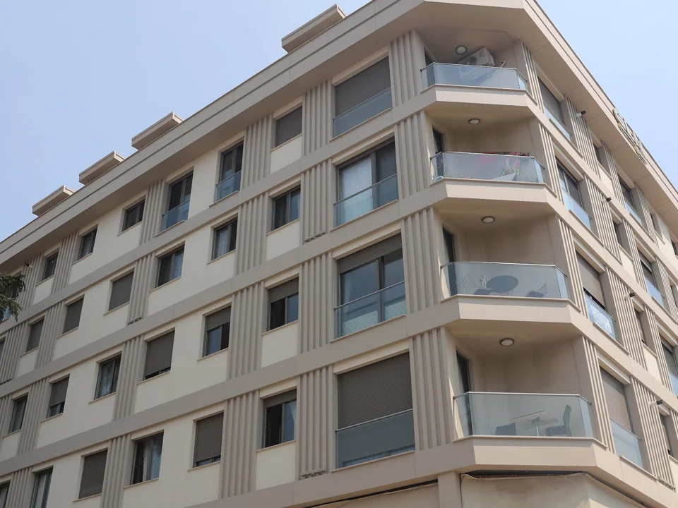 Multi-storey urban apartment building clad in warm beige painted smooth fibre cement exterior panels and window trims
