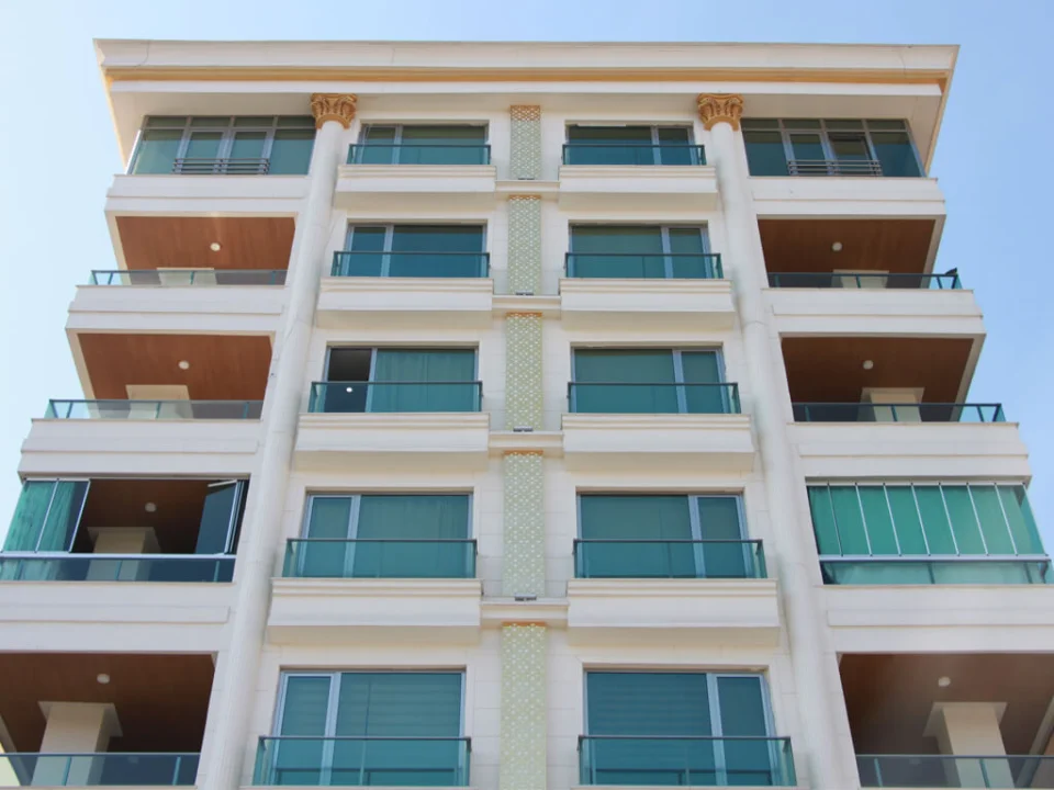 Symmetric residential building elevation featuring light cream painted smooth fibre cement facade panels and warm wood-look balcony soffits