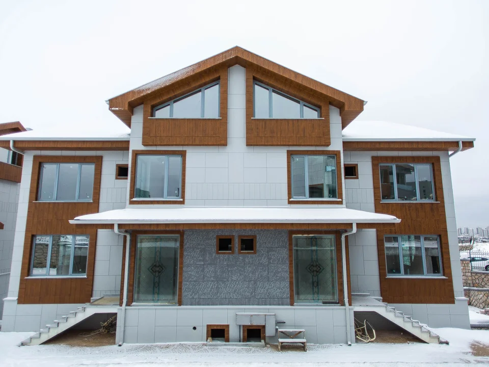 Two-storey residence in snowy winter climate clad in warm wood-grain fibre cement gable trim, white grooved walls and grey stone-textured base panels