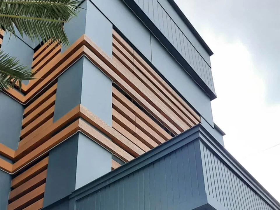 Upward view of coastal hotel facade combining dark slate-textured fibre cement panels and horizontal wood-look accent strips