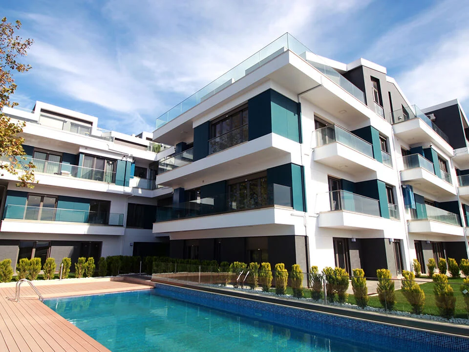 Upscale low-rise residential complex beside a swimming pool featuring crisp white horizontal balcony bands and dark teal-slate textured fibre cement wall panels